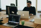 A web developer working on code in a modern office setting with multiple devices.